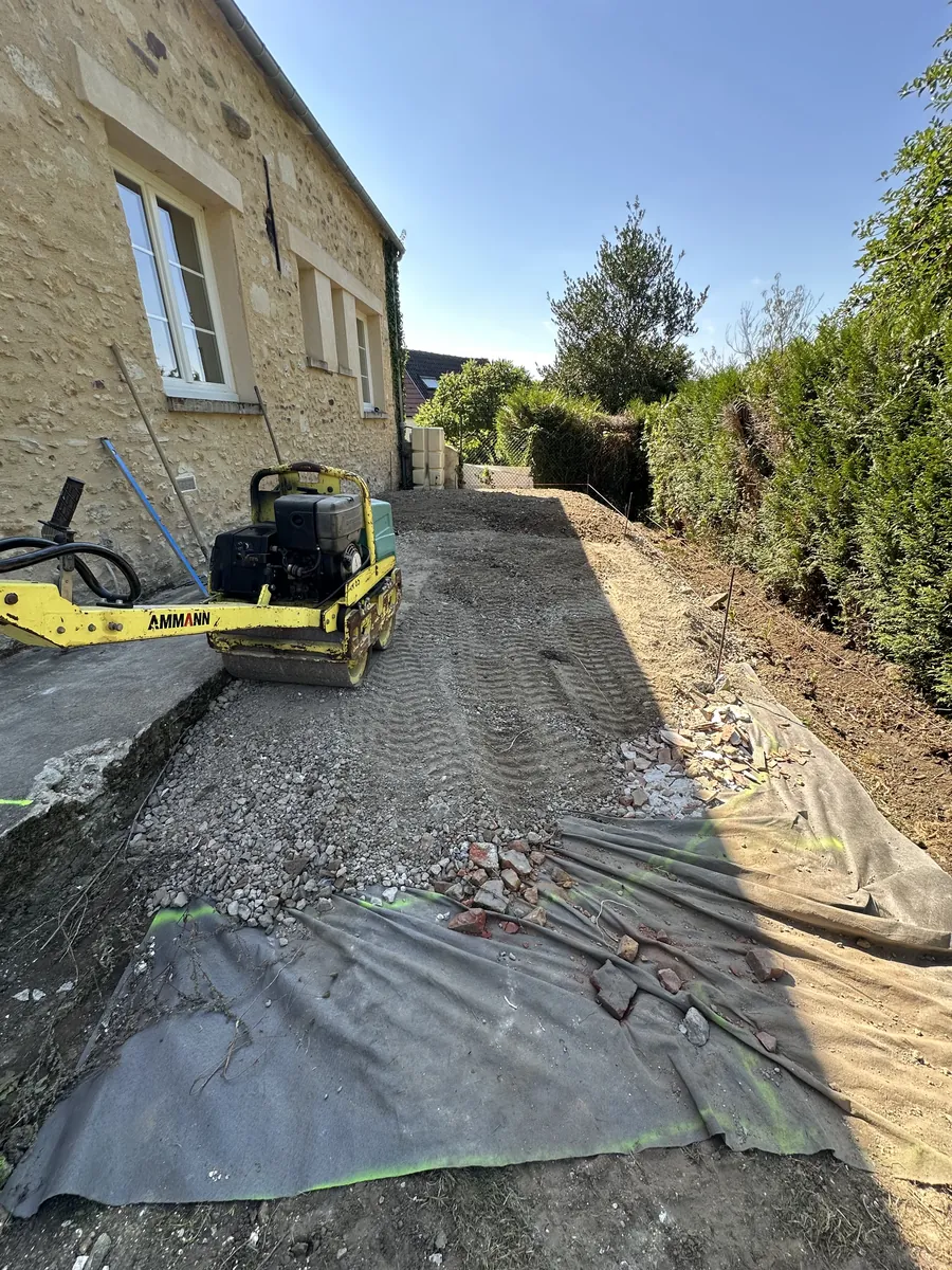 Géotextile déroulé et grave compactée au rouleau le long d'une maison en pierre