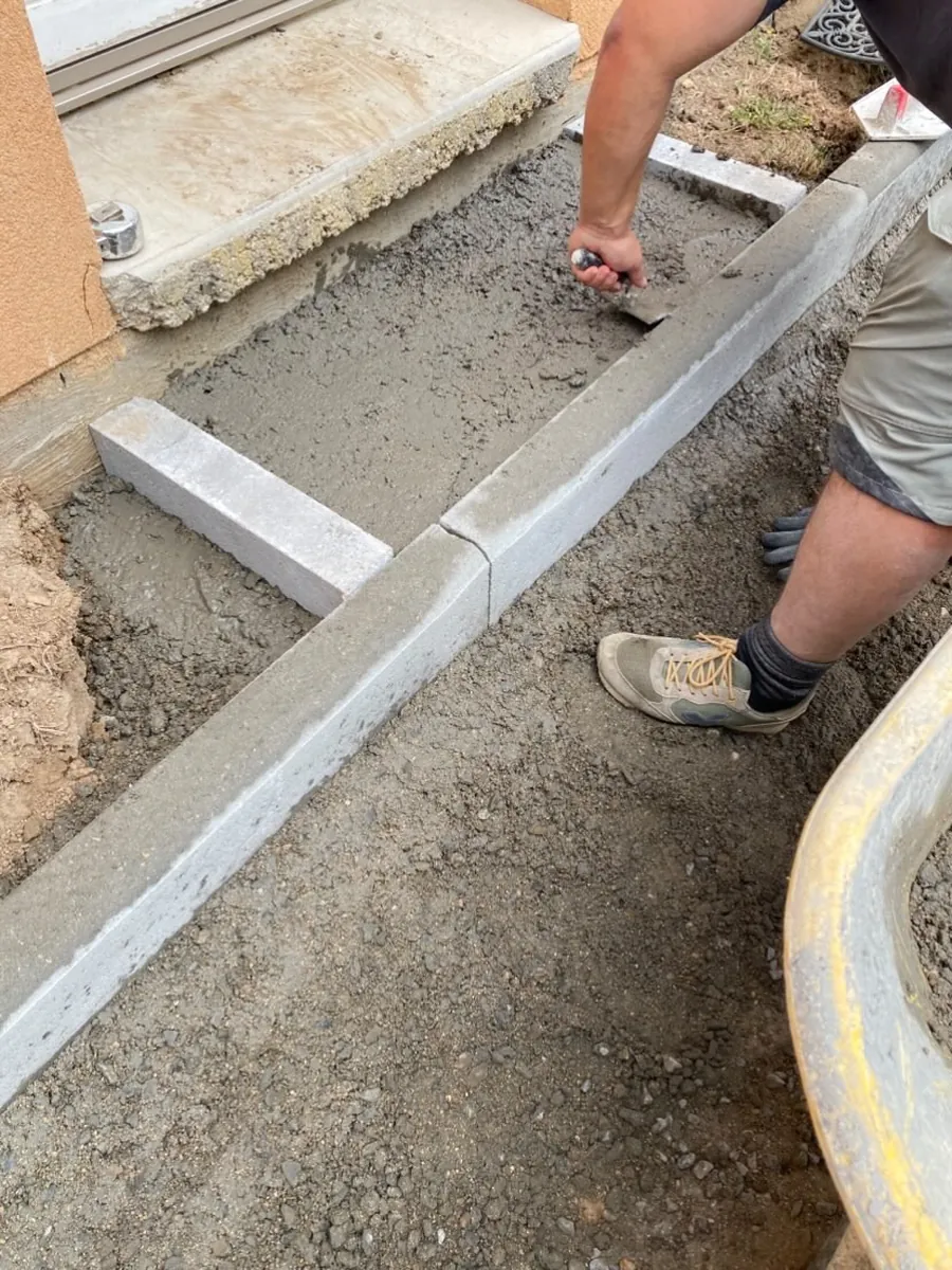 Bordure béton posée sur un lit de béton frais, maintenue à la main