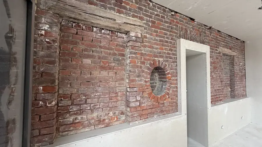 Mur de briques ancien dans une pièce, avec sa porte et son œil-de-bœuf