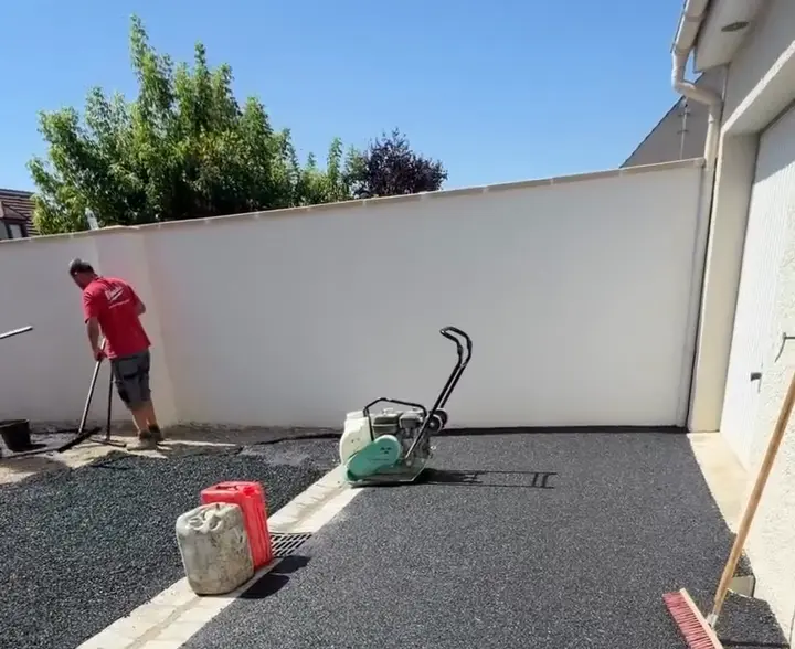 Enrobé noir terminé entre les lignes de pavés, devant le mur de clôture