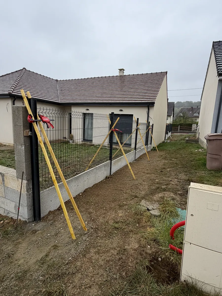 Poteaux de clôture étayés et panneaux rigides en cours de pose