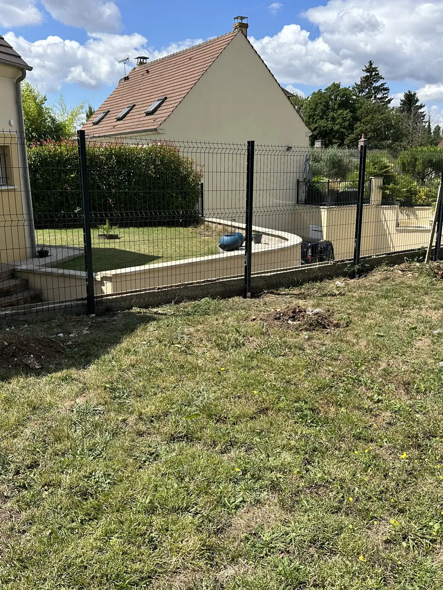 Clôture en panneaux rigides verts sans soubassement, au bord d'un jardin