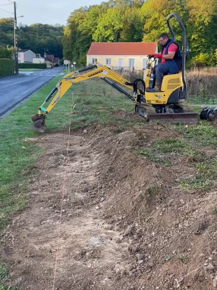 Mini-pelle ouvrant la tranchée de la clôture le long de la route