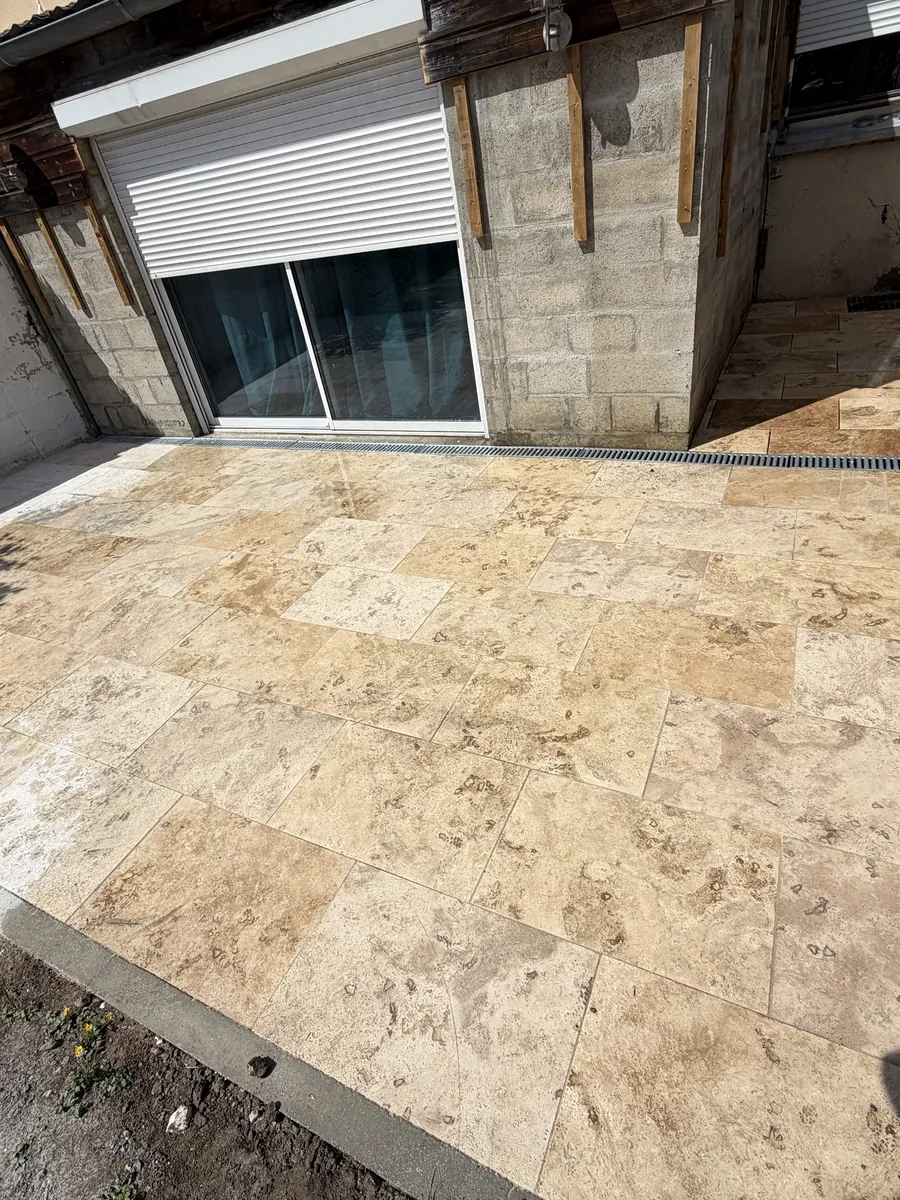 Terrasse en dalles claires terminée avec son caniveau à grille, dans un jardin clos