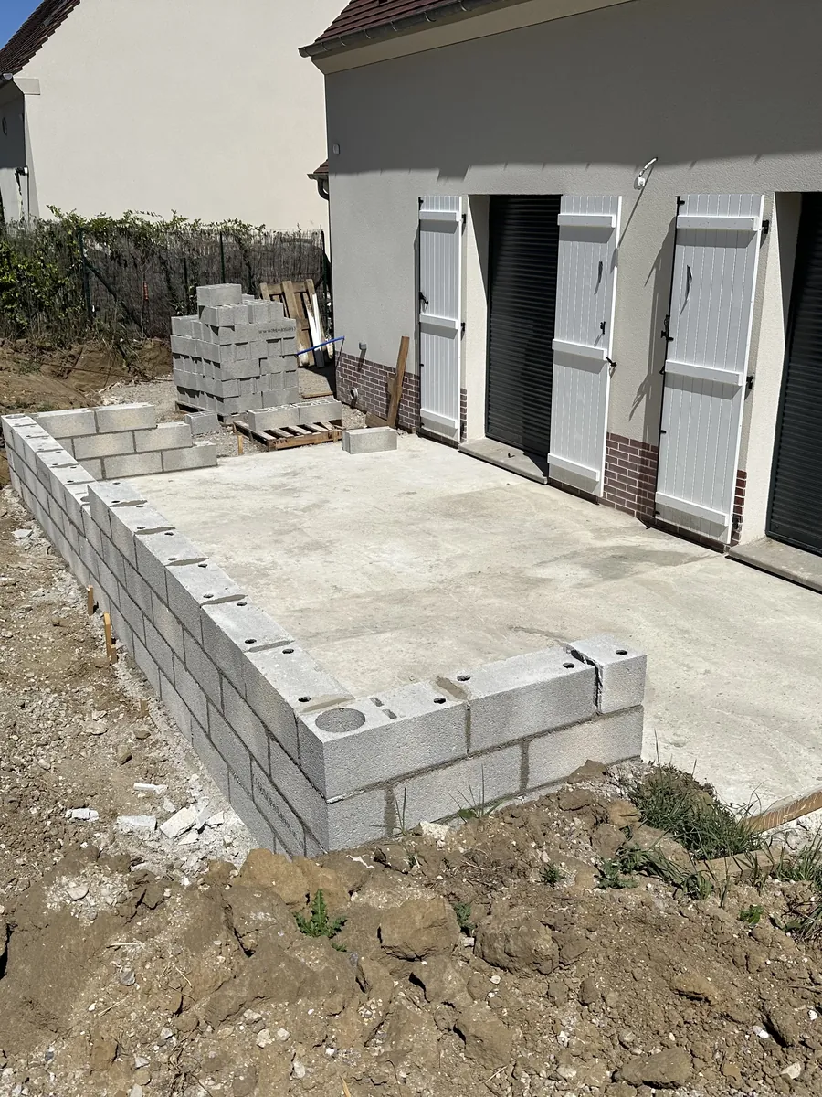Dalle béton coulée devant un garage, premiers rangs de parpaings montés dessus