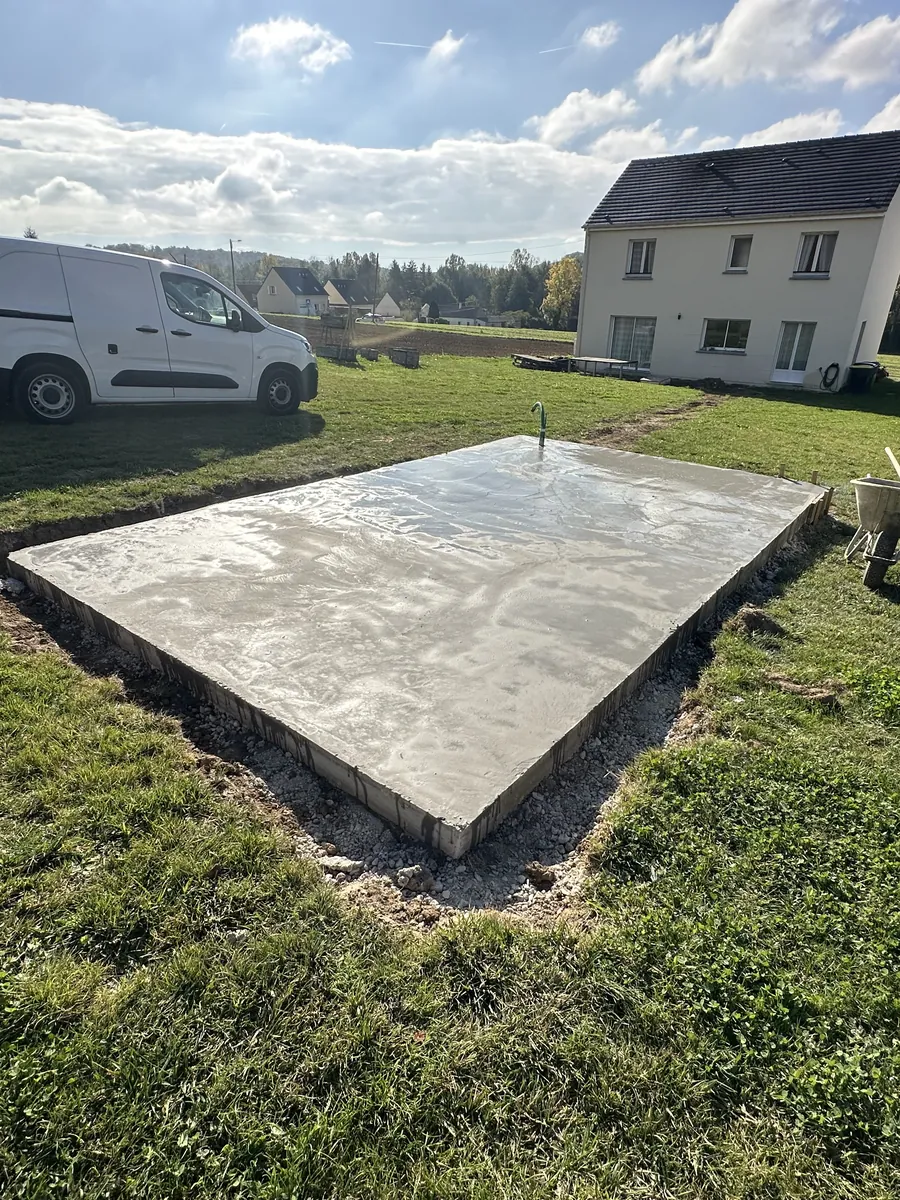 Dalle béton terminée au fond d'un jardin, une camionnette garée dans l'herbe