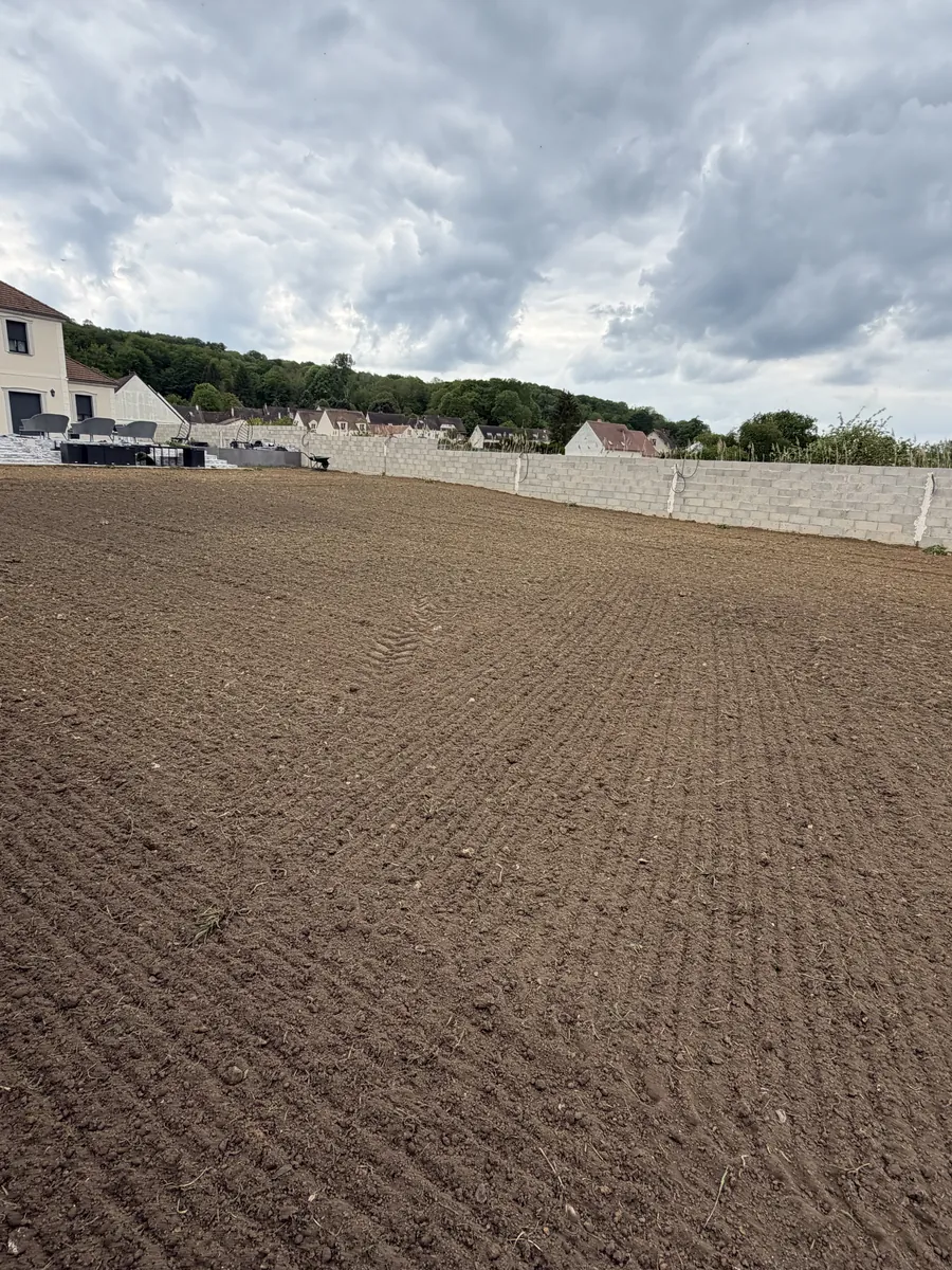 Grand terrain préparé et nivelé jusqu'au mur de clôture, une maison au fond