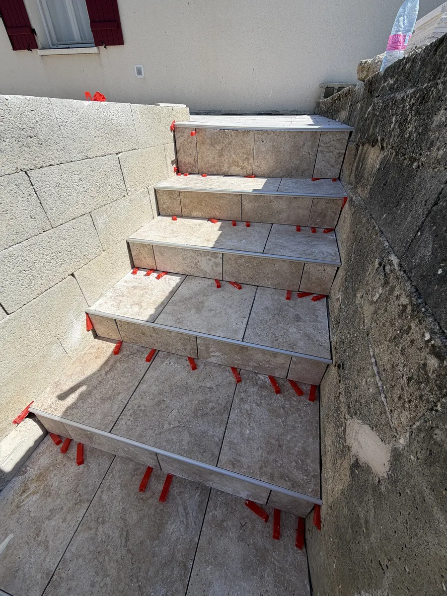 Escalier extérieur carrelé entre deux murs, croisillons rouges encore en place
