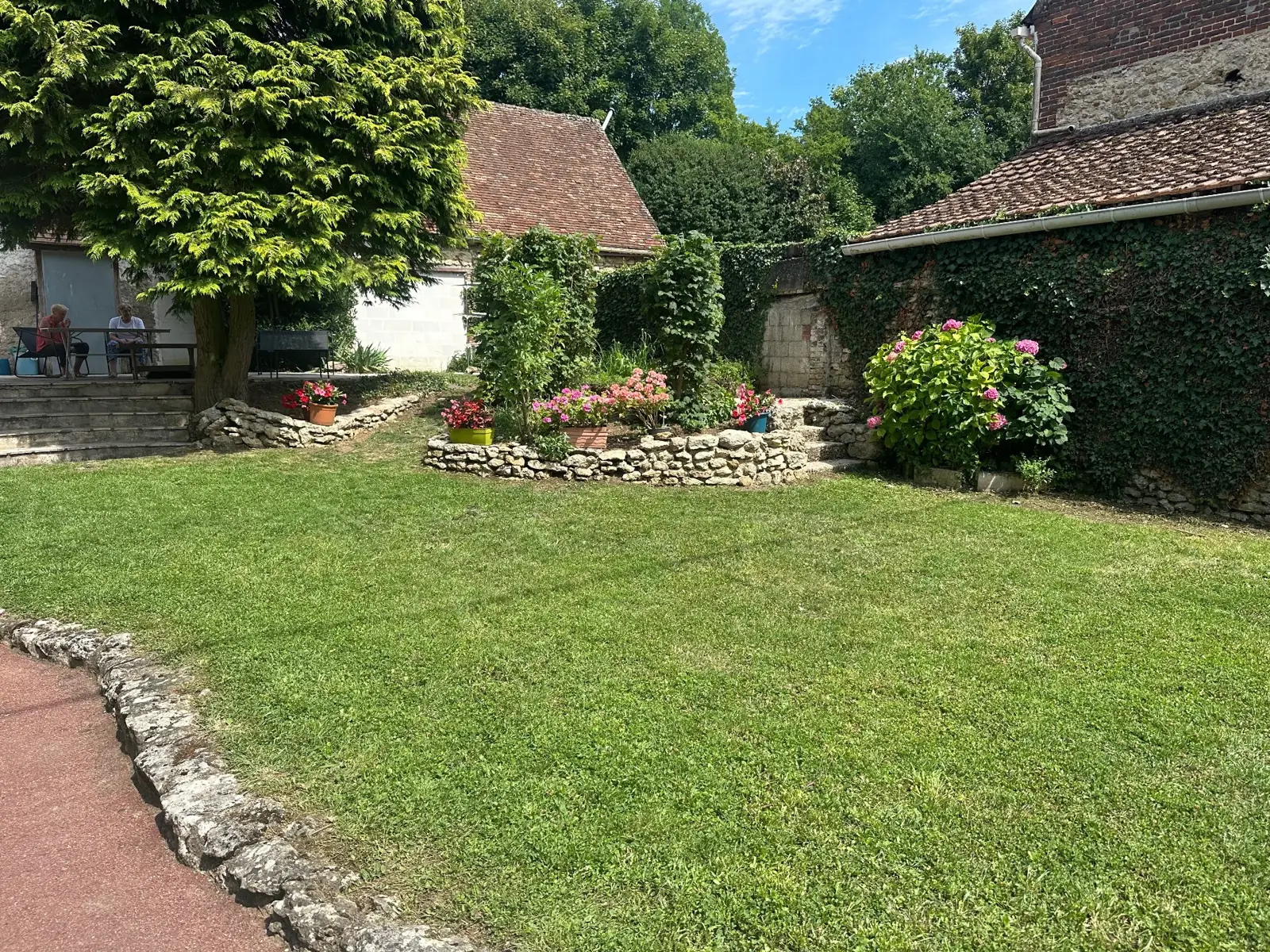 Jardin entretenu, pelouse tondue et massifs fleuris le long d'un muret en pierre