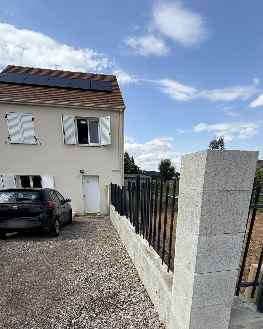 Pilier et muret béton surmontés d'un barreaudage noir, devant une maison