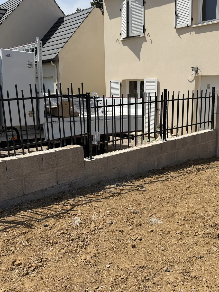 Muret béton surmonté d'un barreaudage noir devant une maison neuve