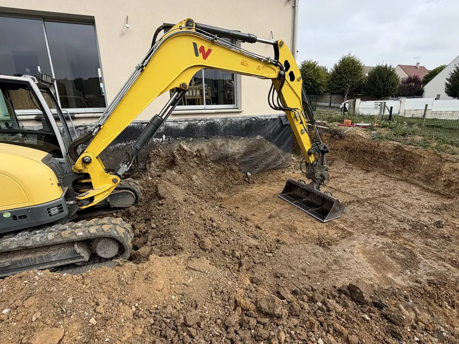 Pelleteuse jaune en terrassement au pied d'une maison neuve