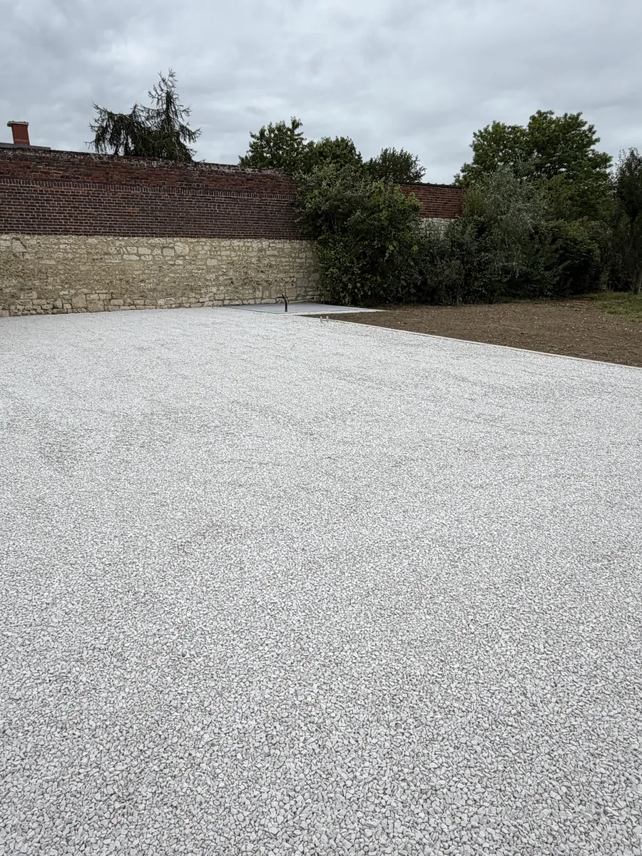 Grand stationnement en gravillon blanc bordé de pavés devant des garages