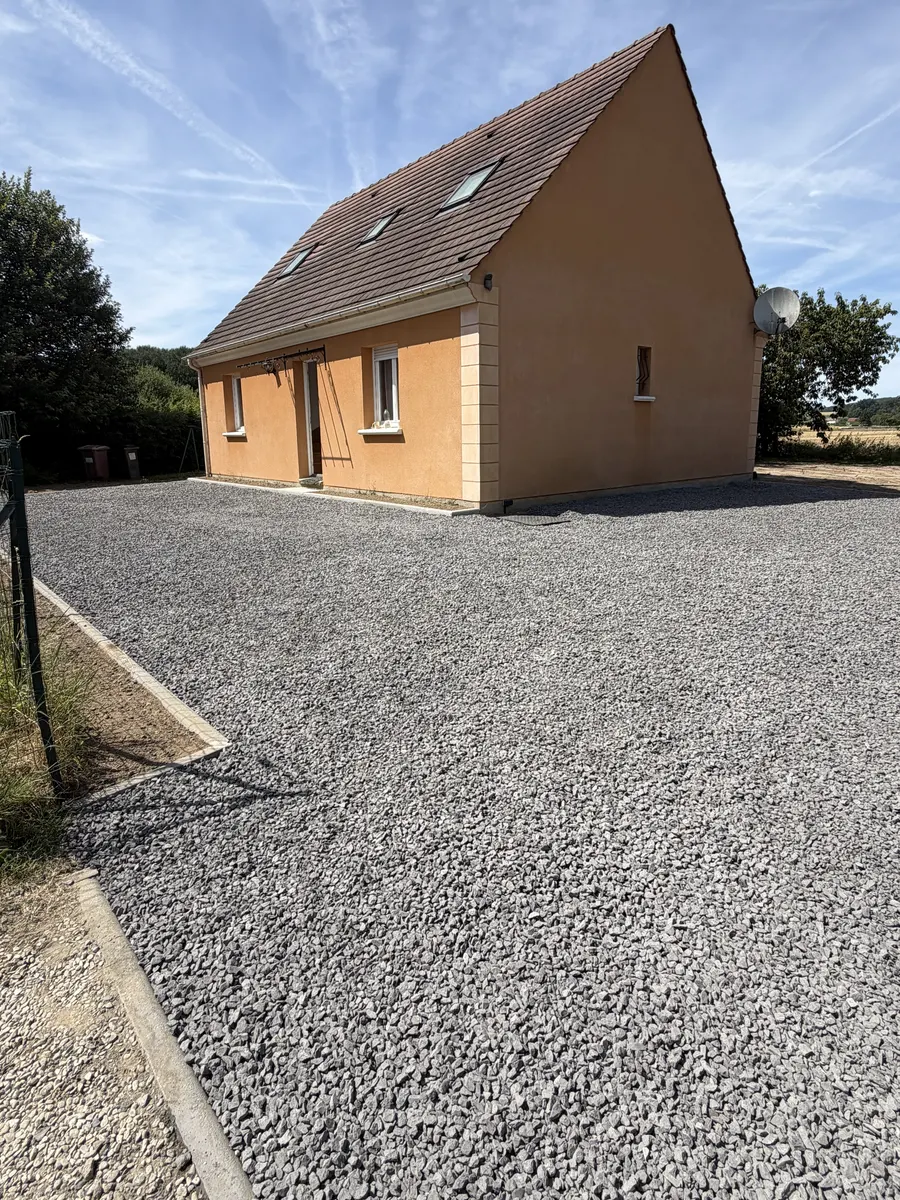 Stationnement en gravillons gris devant une maison orange, bordé de bordures