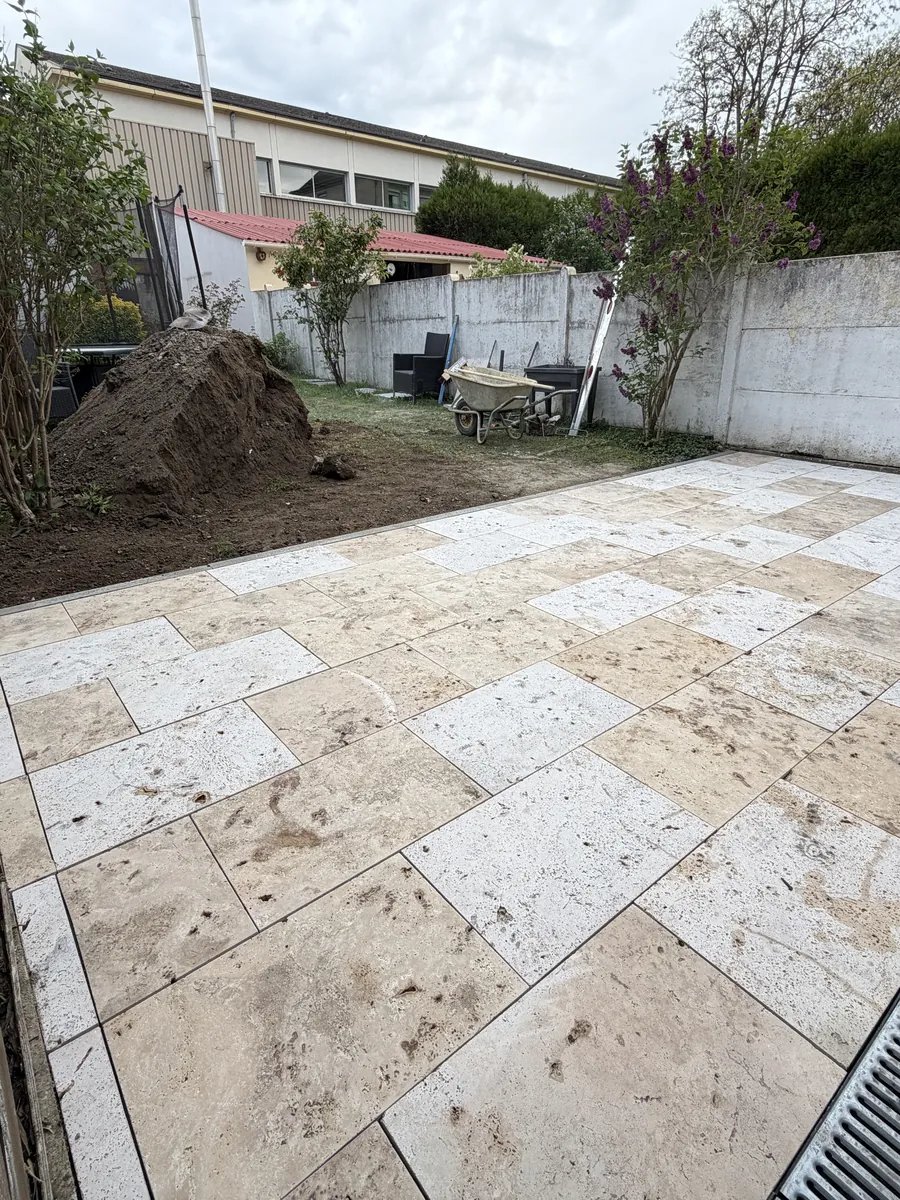 Terrasse en dalles claires avec un caniveau à grille, dans un jardin clos